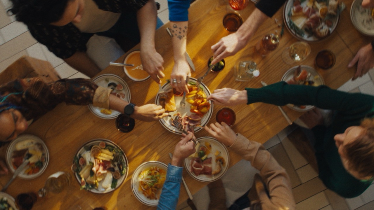 Friends sharing beautifully plated dishes around a restaurant table, passing food to each other in a warm social dining atmosphere